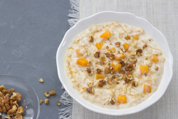 Pumpkin oatmeal with honey and nuts, milk in a milkman, walnuts on a gray background. healthy delicious homemade breakfast. free space