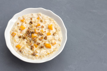 Pumpkin oatmeal with honey and nuts, milk in a milkman, walnuts on a gray background. healthy delicious homemade breakfast. free space