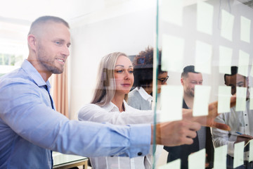 Fototapeta premium Group Of Businesspeople Sticking Adhesive Notes On Glass Wall
