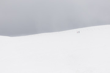 A very minimalistic view of two distant people over a mountain covered by snow, near a fence