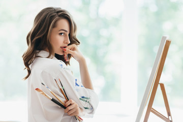 Beautiful woman artist with brushes posing in her studio