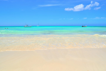 coast of the Caribbean Sea, white sand, beautiful azure water of the sea, boats and boats on the horizon, blue sky covered with light white clouds