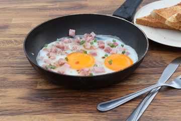 pan fried egg with ham and bread on wood background for breakfast, top view