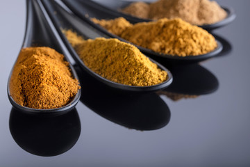 Small black bowls of Indian spices on black reflective background .