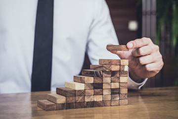Risk To Make Business Growth Concept With Wooden Blocks, hand of man has piling up and stacking a...