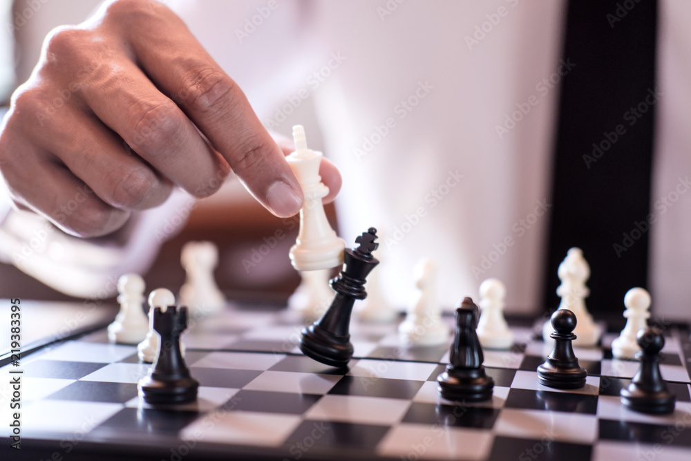 Wall mural Hand of confident businessman use king chess piece white playing chess game to crash overthrow the opposite team and development analysis new strategy plan, business strategy for win and success