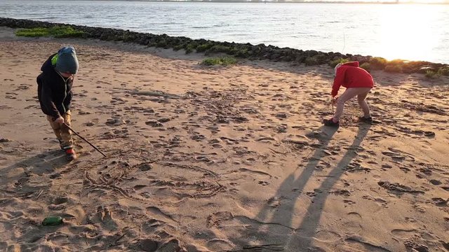 Little brother and sister write words in the sand together