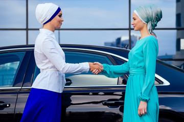 two beautiful girlfriends caucasian Muslim office lady discussing with a businesswoman partner shawl and turban on head perfect skin and makeup shaking hands. team work and a successful deal concept