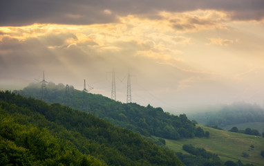 foggy autumn countryside in mountains. power line tower on the forested hill touch the cloud. beautiful golden light
