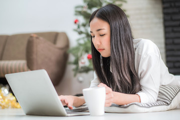 Happy young Asian business woman using laptop by laying on the floor at home, business online shopping. 