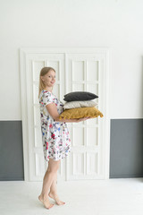 Fototapeta premium Lifestyle concept. A young woman is standing with pillows at home. Stability and coziness.