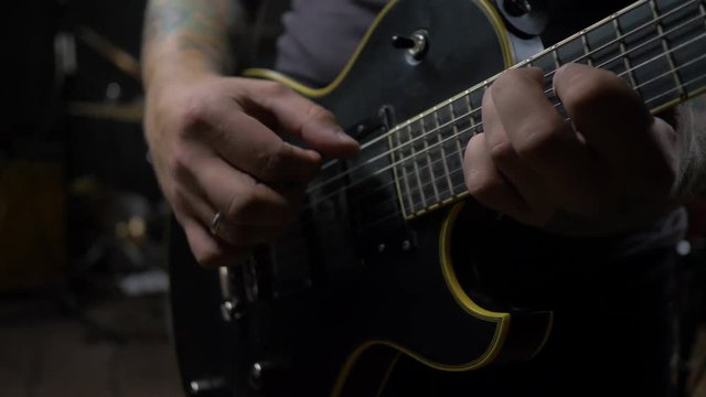 a young man with tattoos plays an electric guitar in a dark room