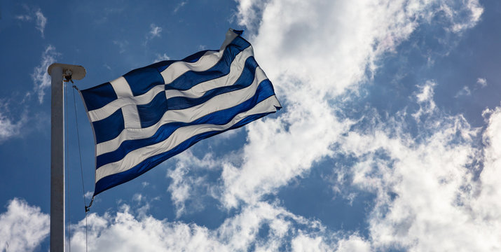 Greek flag on flagpole waving on blue sky background