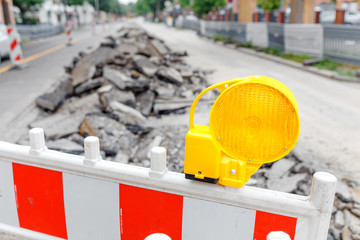 Close-up on a fence with a yellow lamp on a closed street for repair of an asphalt on a city road