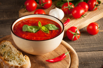 Fresh, healthy tomato soup with basil, pepper, garlic, tomatoes and bread on wooden background. Spanish gazpacho soup.