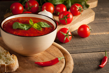 Fresh, healthy tomato soup with basil, pepper, garlic, tomatoes and bread on wooden background. Spanish gazpacho soup.