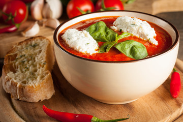 Fresh, healthy tomato soup with basil, pepper, garlic, tomatoes and bread on wooden background. Spanish gazpacho soup.