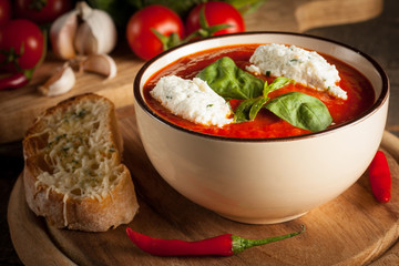 Fresh, healthy tomato soup with basil, pepper, garlic, tomatoes and bread on wooden background. Spanish gazpacho soup.