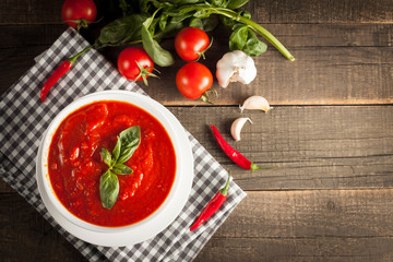 Fresh, healthy tomato soup with basil, pepper, garlic, tomatoes and bread on wooden background. Spanish gazpacho soup.