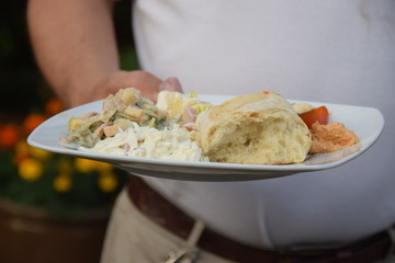 Grillteller mit Bratwurst, Weißbrot und Kartoffelsalat in der Hand eines Partygastes