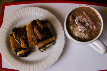 White cup with coffee on a tray with a plate with rolls with poppy seeds