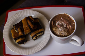 White cup with coffee on a tray with a plate with rolls with poppy seeds