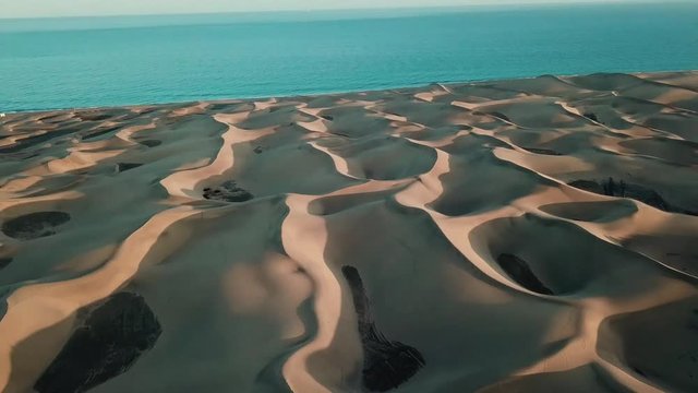 Aerial view of the horizon with sand desert, dunes and the ocean on background. Flying over sand dunes in a desert during sunset. Sand texture. Gran Canaria