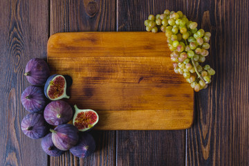 Wooden kitchen board with fig fruits and grapes on it.
