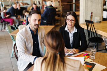 Business meeting in coffee shop. Three young motivated colleagues discussing about new ideas and problems at work.