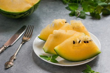 Slices of a yellow watermelon on a white plate, knife, fork and greens.