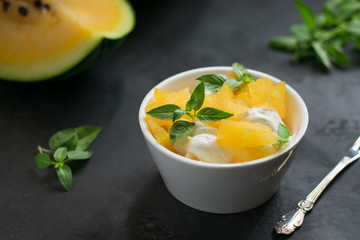 Pieces of yellow watermelon with ice cream in a white cup, fork, green leaves and watermelon