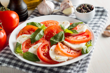 Photo of Caprese Salad with tomatoes, basil, mozzarella, olives and olive oil on wooden background. Italian traditional caprese salad ingredients. Mediterranean, organic and natural food concept.