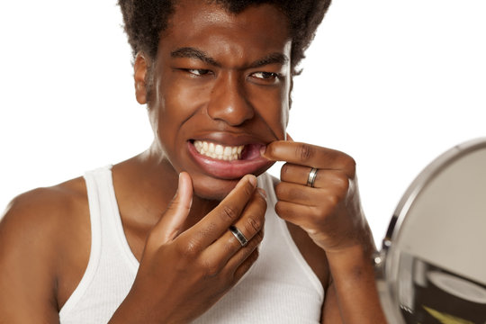 young handsome afro american guy checking his teeth in mirror on white background