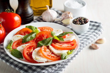 Photo of Caprese Salad with tomatoes, basil, mozzarella, olives and olive oil on wooden background. Italian traditional caprese salad ingredients. Mediterranean, organic and natural food concept.