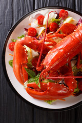 Luxury food recipe: boiled lobster with fresh vegetable salad close-up on a plate on a black table. Vertical top view