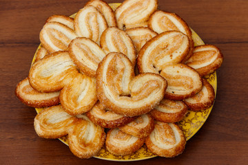 Palmier biscuits - french cookies made of puff pastry (also called palm leaves, elephant ears or french hearts) in a plate on wooden table