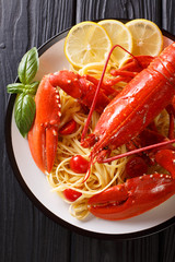 Served spaghetti pasta with red lobster, tomatoes, lemon and fresh herbs close-up on a black background. Vertical top view