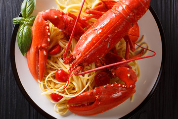 Luxury food recipe: spaghetti and boiled lobster, tomatoes, lemon and fresh herbs close-up on a black background. Horizontal top view