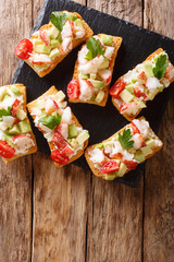 Toasted sandwiches with lobster, avocado, tomatoes and cream cheese close-up on the table. Vertical top view, rustic