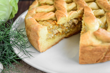 Homemade pie with cabbage, carrot, onion and meat on wooden background.