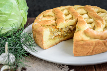 Homemade pie with cabbage, carrot, onion and meat on wooden background.