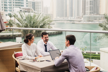 Fototapeta premium Business meeting on modern balcony in Dubai Marine . Three people representing their companies and talking about cooperation.