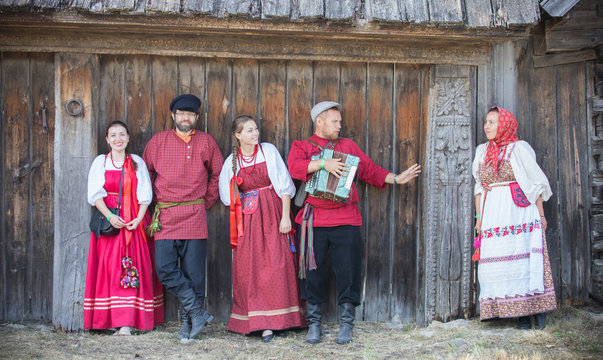 A group of people in russian national costumes stand in a row and pose for the camera against a wooden gate