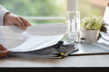Businessman hands holding pen for working in Stacks of paper files searching information business report papers and piles of unfinished documents achieves on laptop computer desk in modern office