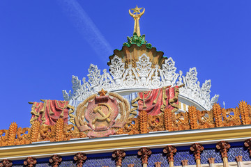 Fototapeta na wymiar Coat of arms of Ukrainian SSR against gilded spire with soviet star on facade of pavilion on VDNH in Moscow on a blue sky background in sunny summer morning