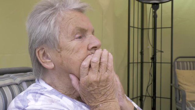 Elderly woman looking apprehensive with her hands over her face