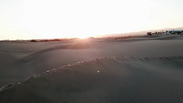 Aerial: camera flies over a desert in sunset light. Horizontal view of endless sand dunes of a desert with sun setting. Gran Canaria