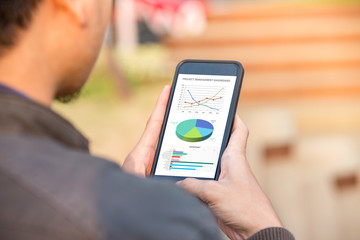 Project management dashboard concept. Man holding phone with excel project dashboard on screen.