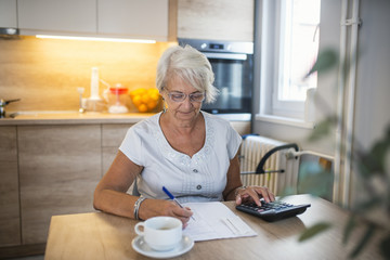 Senior woman checking pension approval certificate with calculator at home