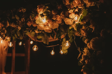 Closeup view of top of beautiful floral night wedding decorations with soft light of lamps. Outdoor reception holiday decor. Horizontal color photography.